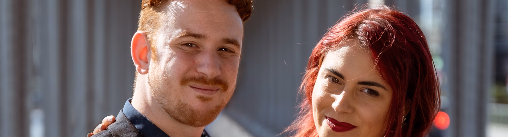 Un homme et une femme souriants posent ensemble à l'extérieur, fond urbain flou.