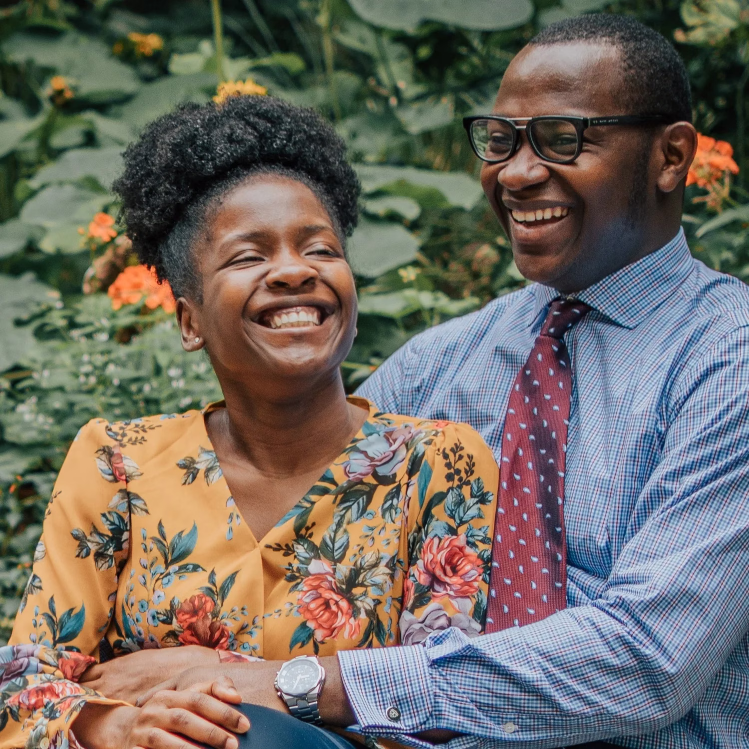 Un couple souriant avec une femme en robe fleurie jaune et un homme en chemise bleue et cravate rouge.