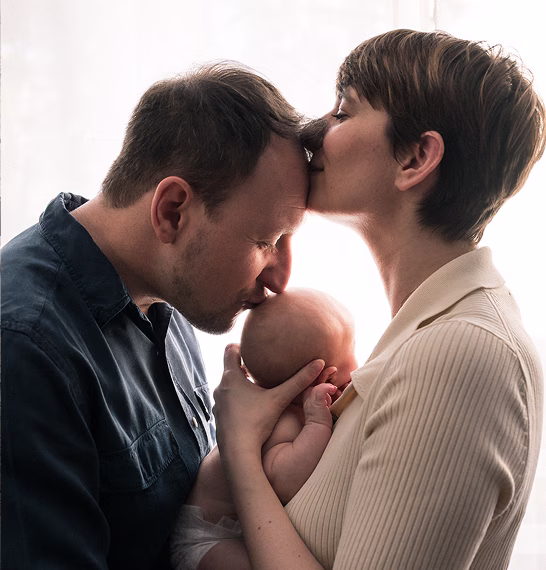 Un homme embrasse la tête d'un bébé tenu par une femme qui lui pose un baiser sur le front.