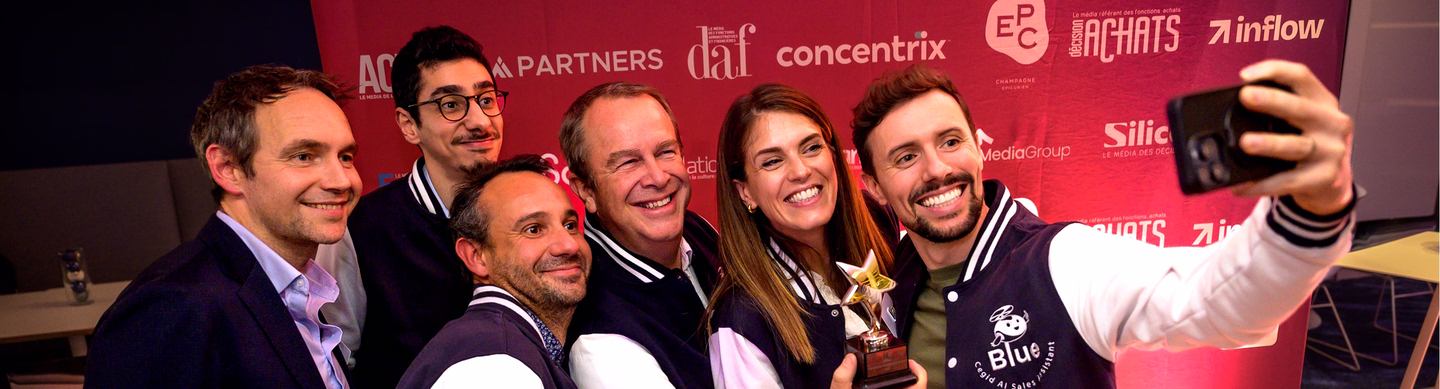 Groupe souriant prenant un selfie, une femme tenant un trophée étoile lors d'un événement.