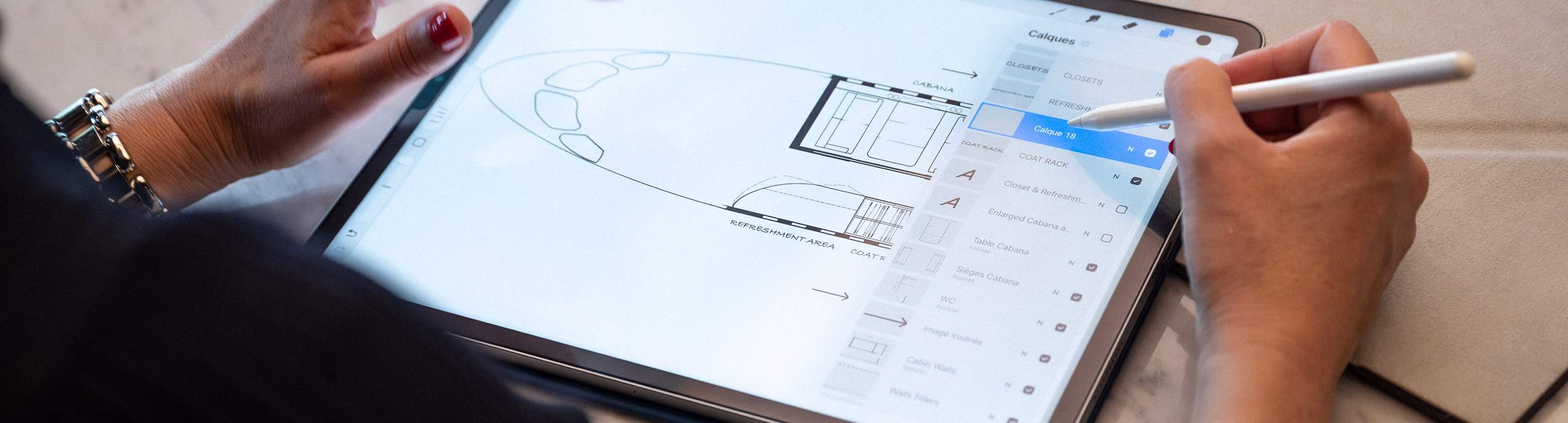 Main de femme utilisant un stylet sur une tablette affichant un plan architectural numérique.