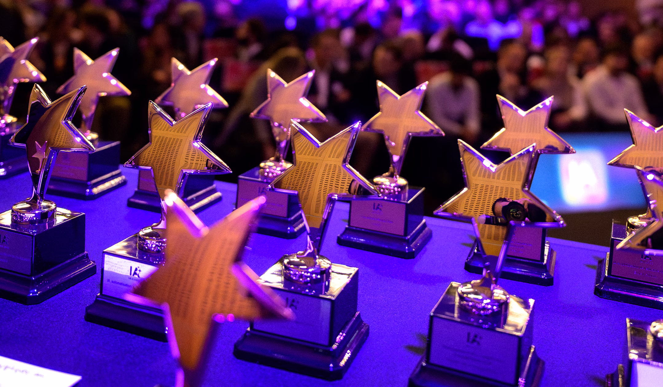 Plusieurs trophées étoilés en métal brillant sur une table bleue lors d'une cérémonie.