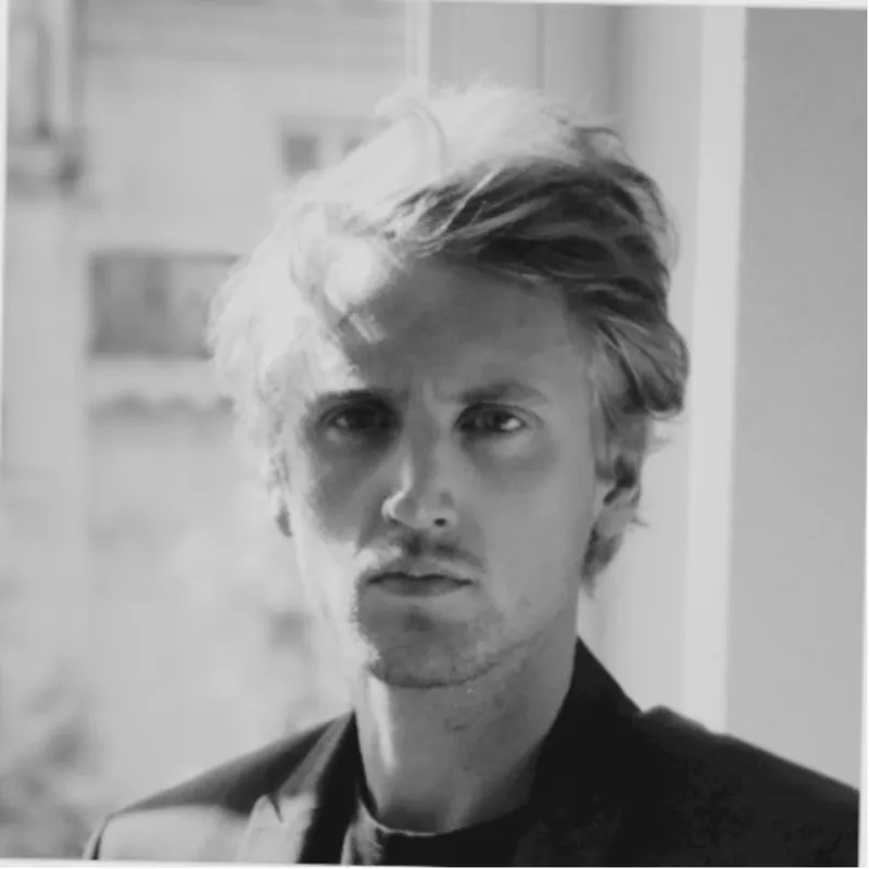 Black and white portrait of a man with light hair wearing a dark jacket looking directly at the camera.