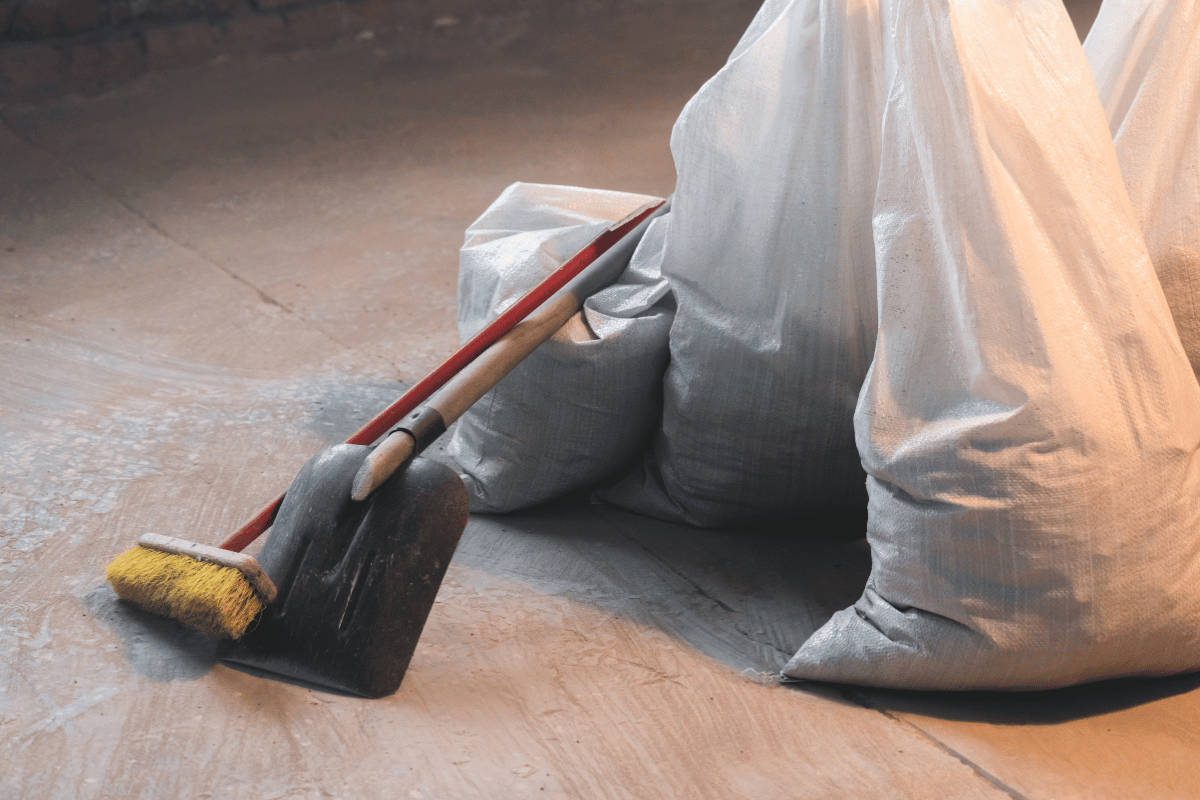 Besen und Kehrblech neben Abdeckfolie auf einer Baustelle
