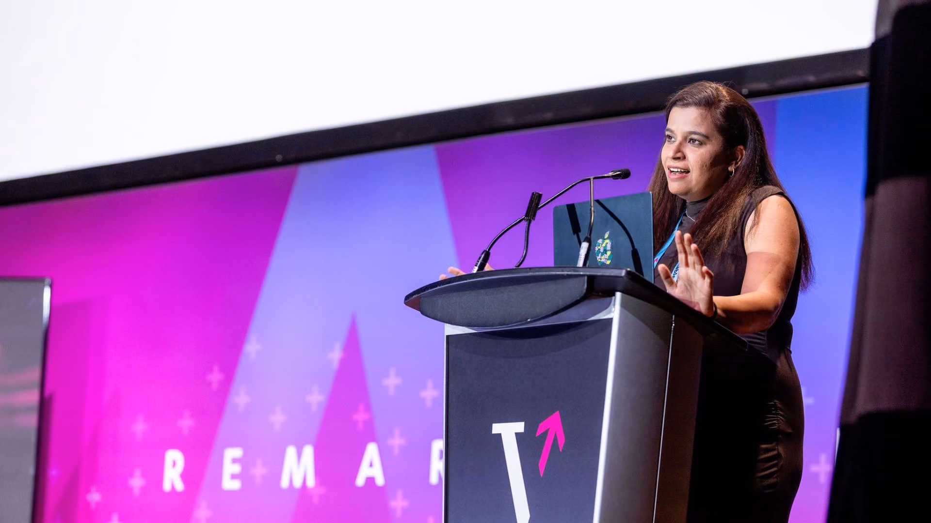 Ankita Upadhyay delivers remarks at the Vector Institute podium on the Remarkable event stage, gesturing with one hand. The pink and purple "Remarkable" backdrop is visible behind her.