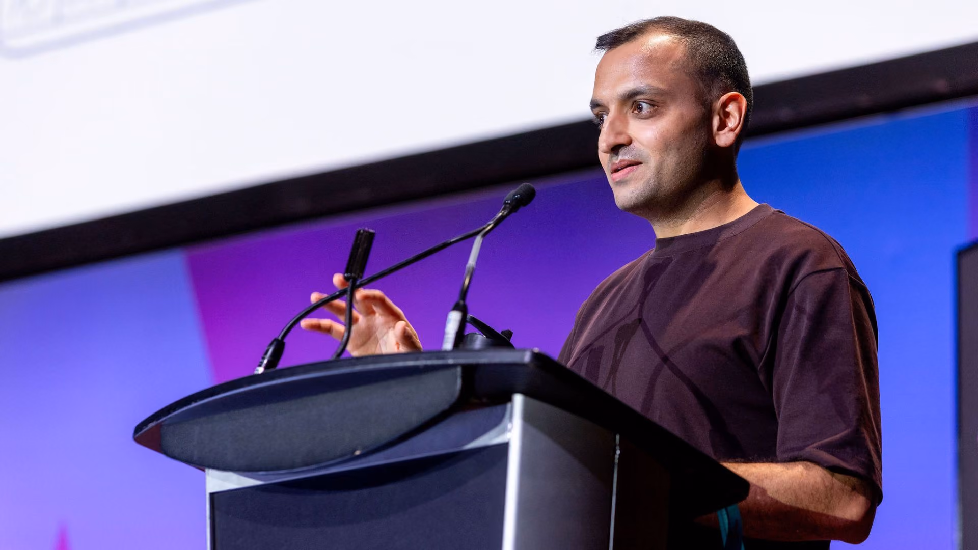 Priyank Jaini speaks at a podium against a purple and pink stage backdrop at a Vector Institute event, gesturing with one hand while engaging the audience.