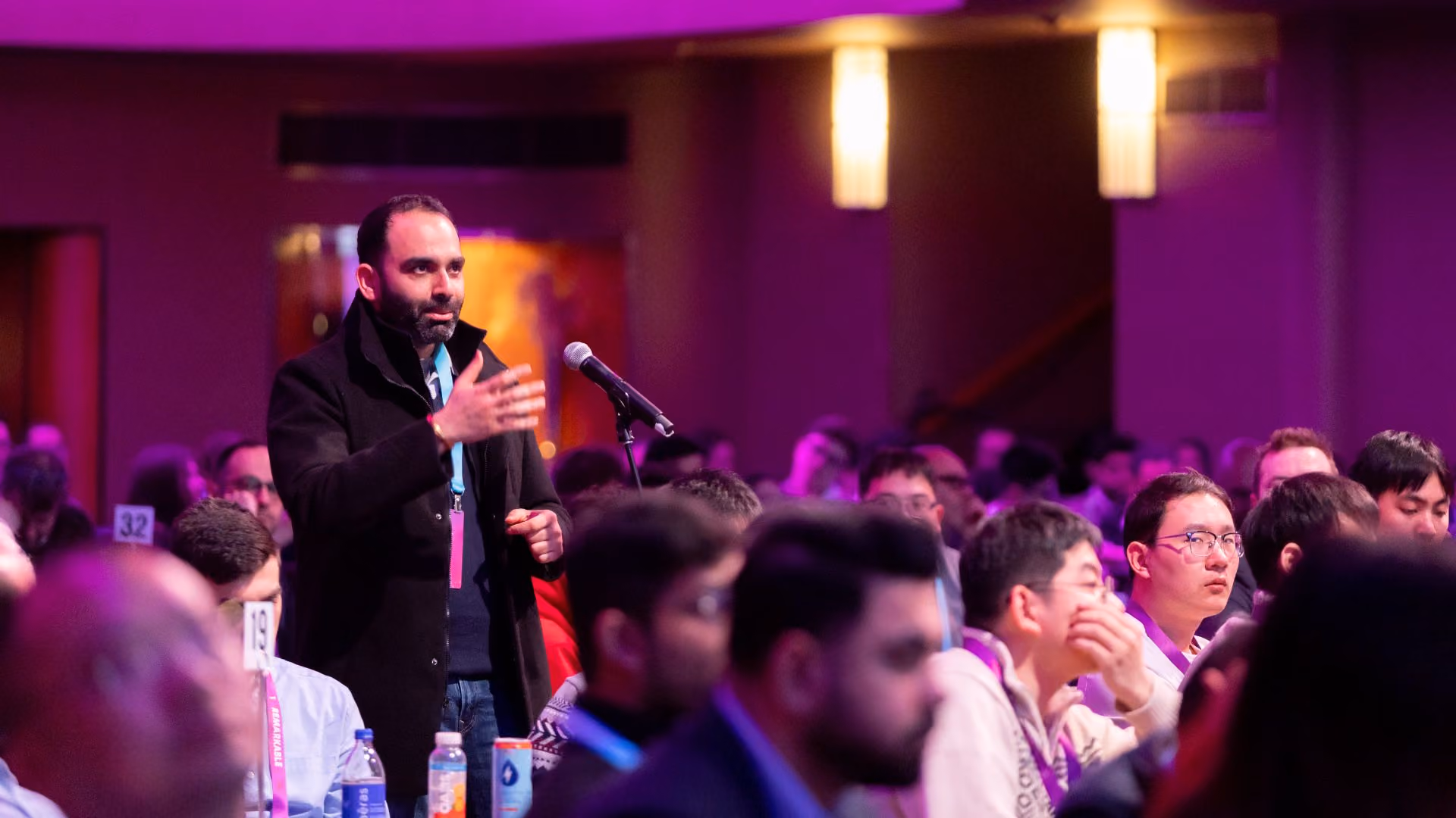 An attendee stands among a large seated audience in a purple-lit ballroom, speaking into a microphone during a Q&A session at a Vector Institute event.