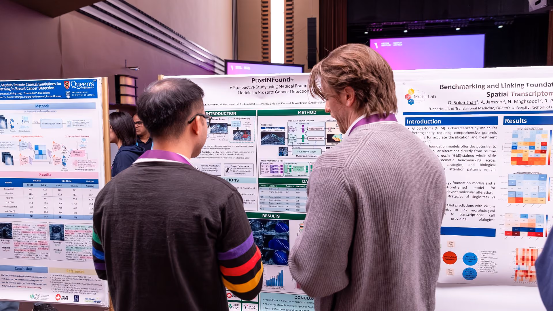 Two attendees examine research posters at a Vector Institute poster session. The visible posters include "ProstNFound+," a prospective study on foundation models for prostate cancer detection and a study on benchmarking foundation models for spatial transcriptomics. The Remarkable event stage is lit in purple in the background.