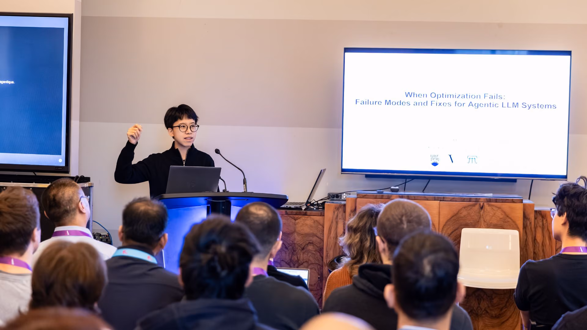 Xiaoxiao Li presents at a podium in a breakout session at a Vector Institute event, one hand raised mid-gesture. The projected slide behind reads "When Optimization Fails: Failure Modes and Fixes for Agentic LLM Systems," with audience members visible in the foreground.