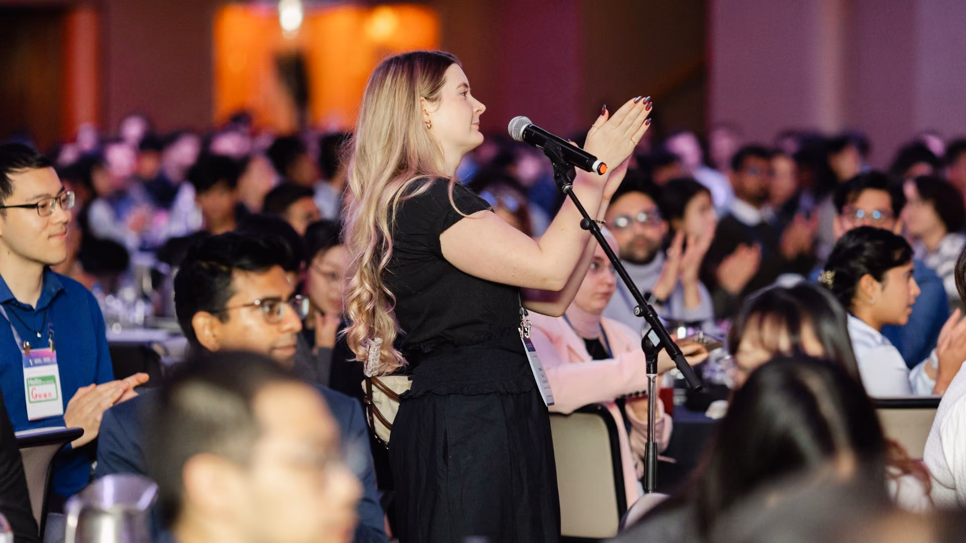 An attendee with long blonde hair stands at a floor microphone in a packed, purple-lit ballroom, gesturing with both hands while speaking during a Q&A session at a Vector Institute event.