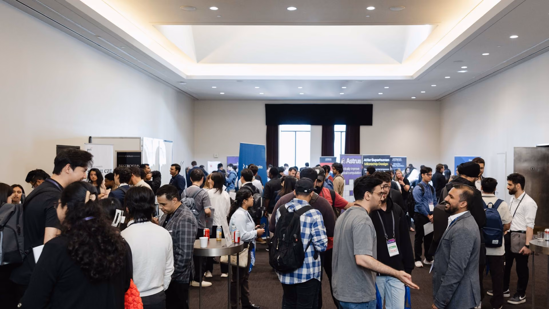 A large, busy networking area at a Vector Institute conference, with dozens of attendees mingling between sponsor booths. Multiple company banners are visible in the background, including one for Astrus.