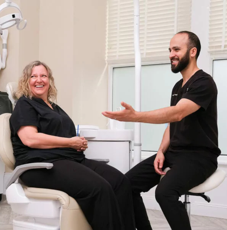Smiling female patient sitting in a dental chair talking to a male dentist in a clinic.