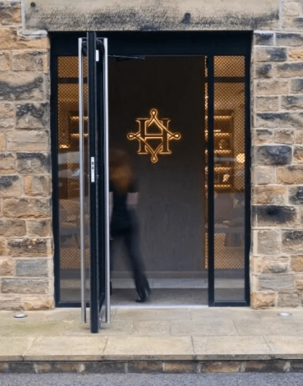 Person entering a stone building through a black-framed glass door with a glowing decorative emblem inside.