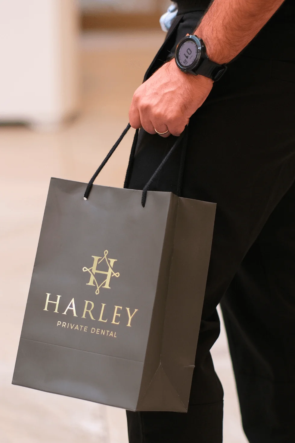 Close-up of a person holding a black shopping bag with gold text reading 'HARLEY PRIVATE DENTAL'.
