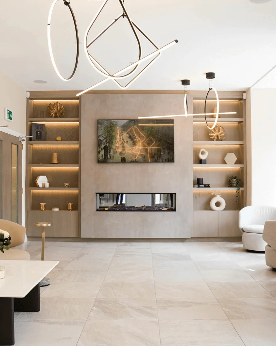 Modern living room featuring geometric pendant lights, built-in shelves with decorative items, a wall-mounted TV, and a rectangular fireplace.