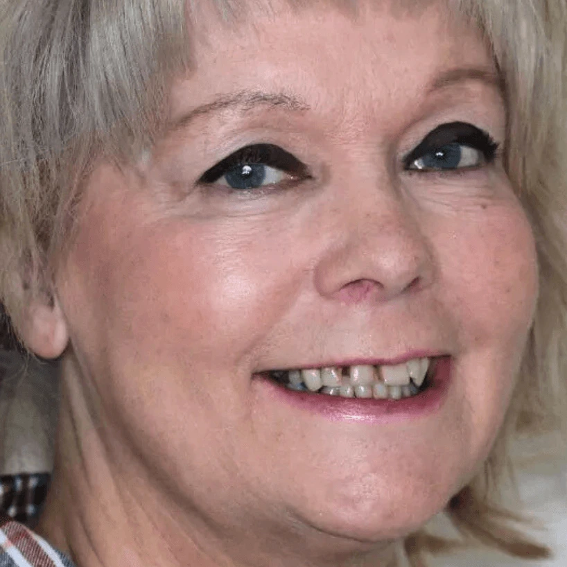 Close-up of a smiling woman with light eye makeup and short blonde hair.