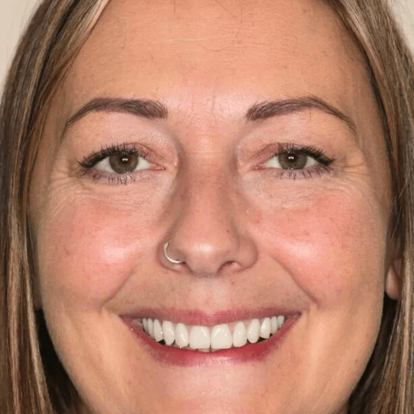 Close-up of a smiling woman with light brown hair, hazel eyes, and a silver nose ring.