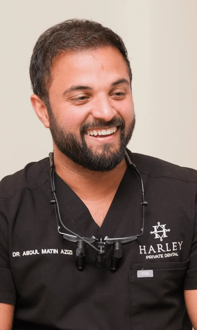 Smiling male dentist wearing black scrubs with magnifying glasses hanging around his neck.
