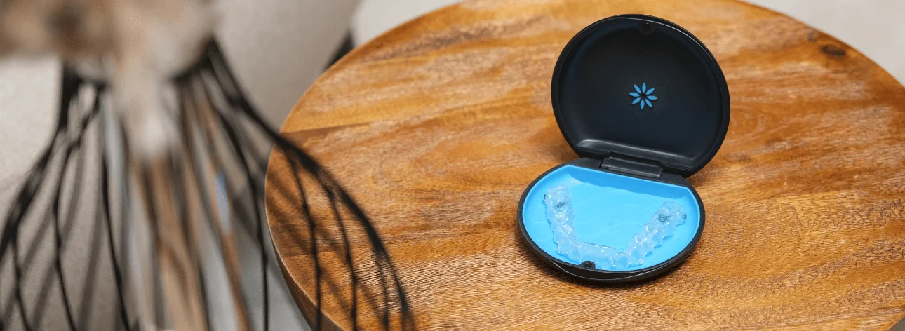 Clear Invisalign aligners in an open black and blue case placed on a round wooden table.