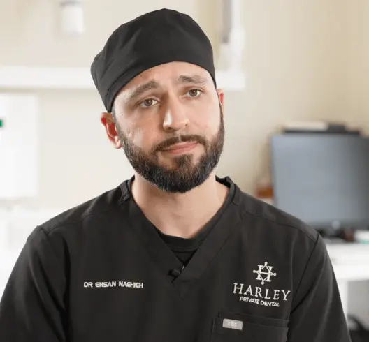Male dentist wearing black scrubs and cap in a dental office.