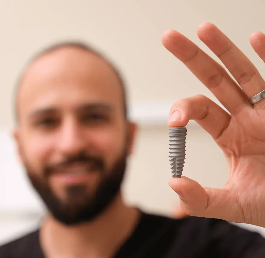 Man holding a small dental implant screw between his fingers, with a blurred background.