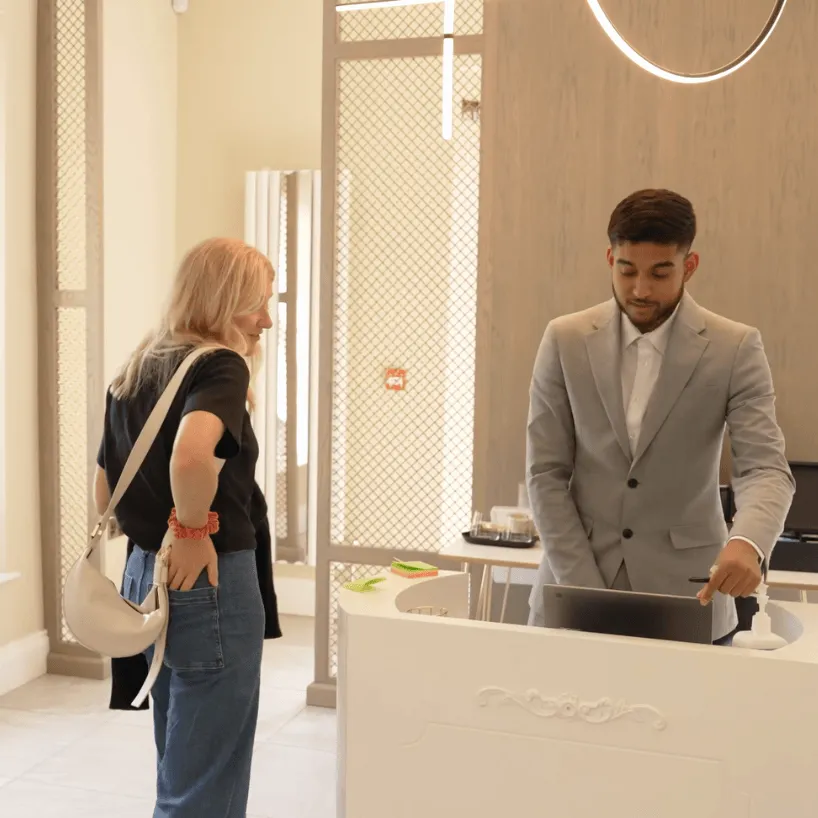 Male dentist in black uniform smiling and talking to a patient in a bright dental clinic.