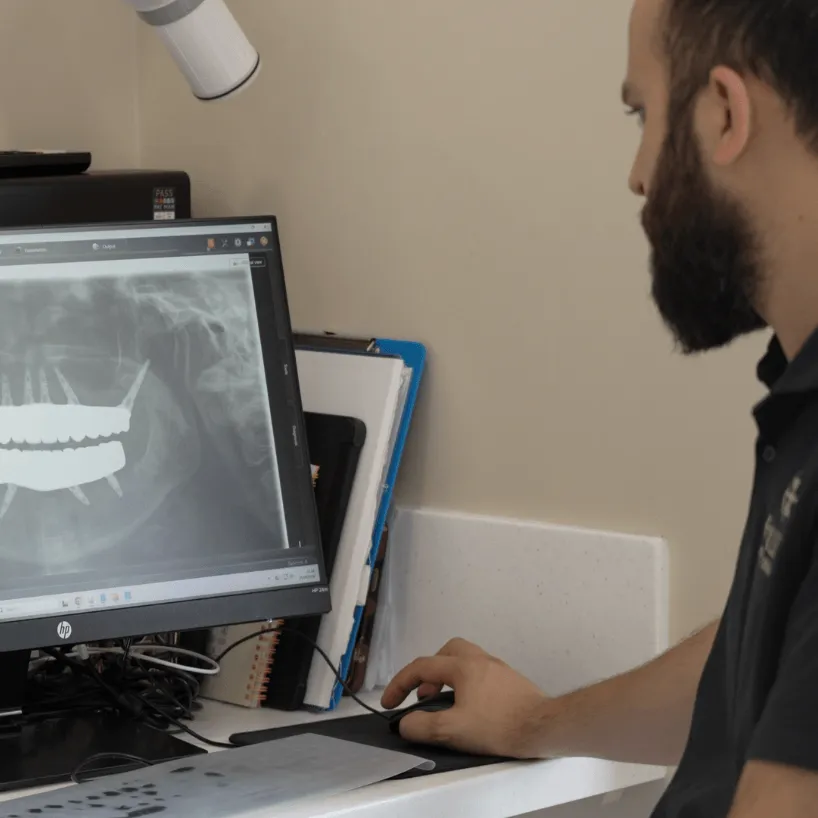 Male dentist in black uniform smiling and talking to a patient in a bright dental clinic.