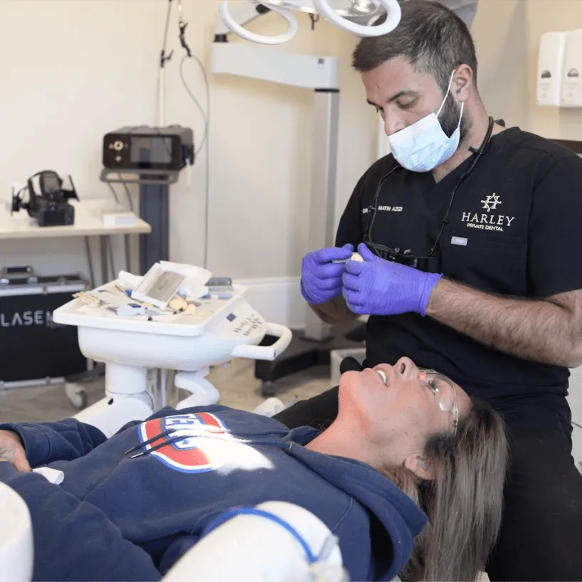 Male dentist in black uniform smiling and talking to a patient in a bright dental clinic.