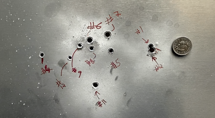 Metal target with eleven bullet holes numbered in red ink and a quarter for scale on the right.