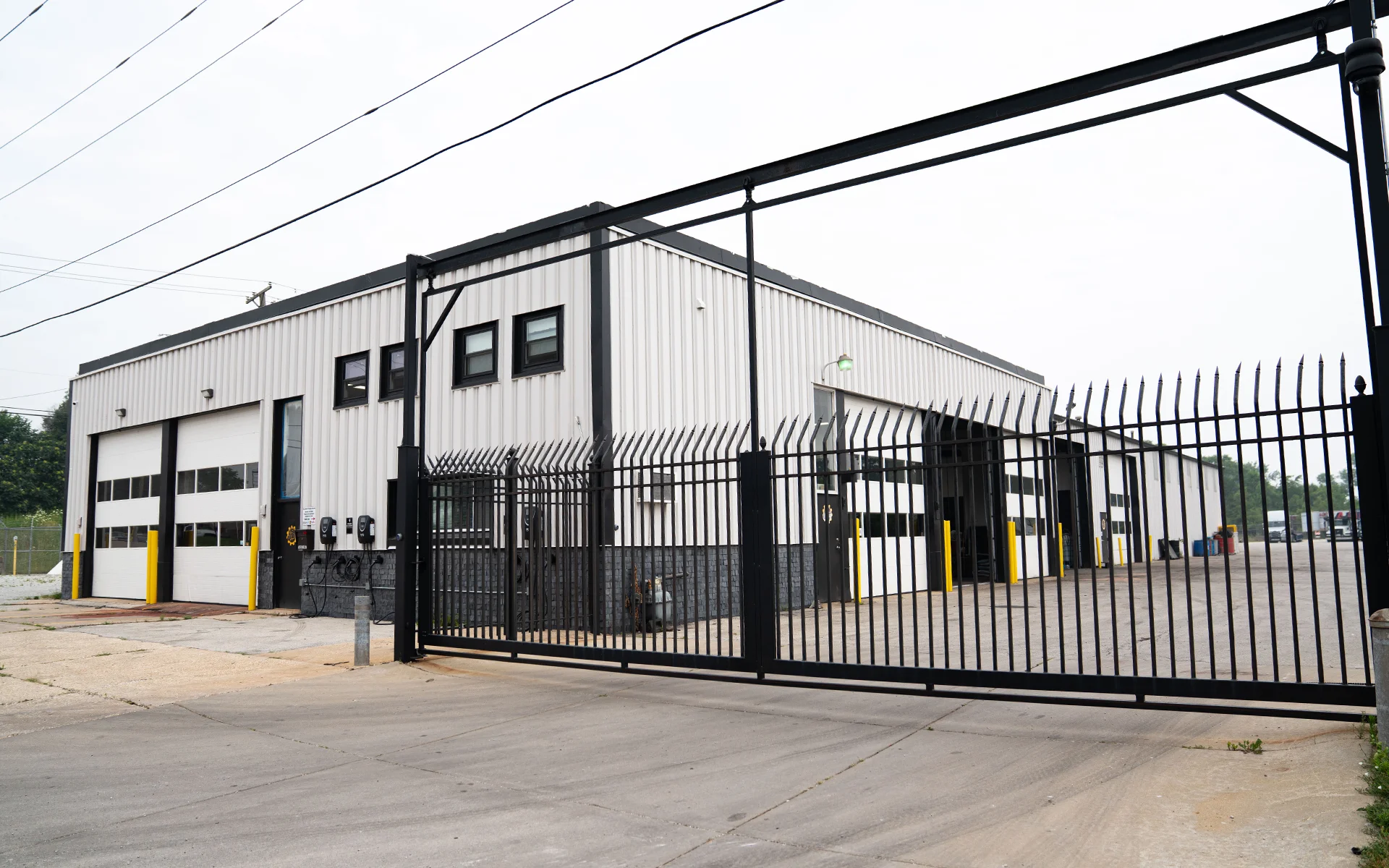 Industrial building with large garage doors behind a tall black metal gate with pointed tops.