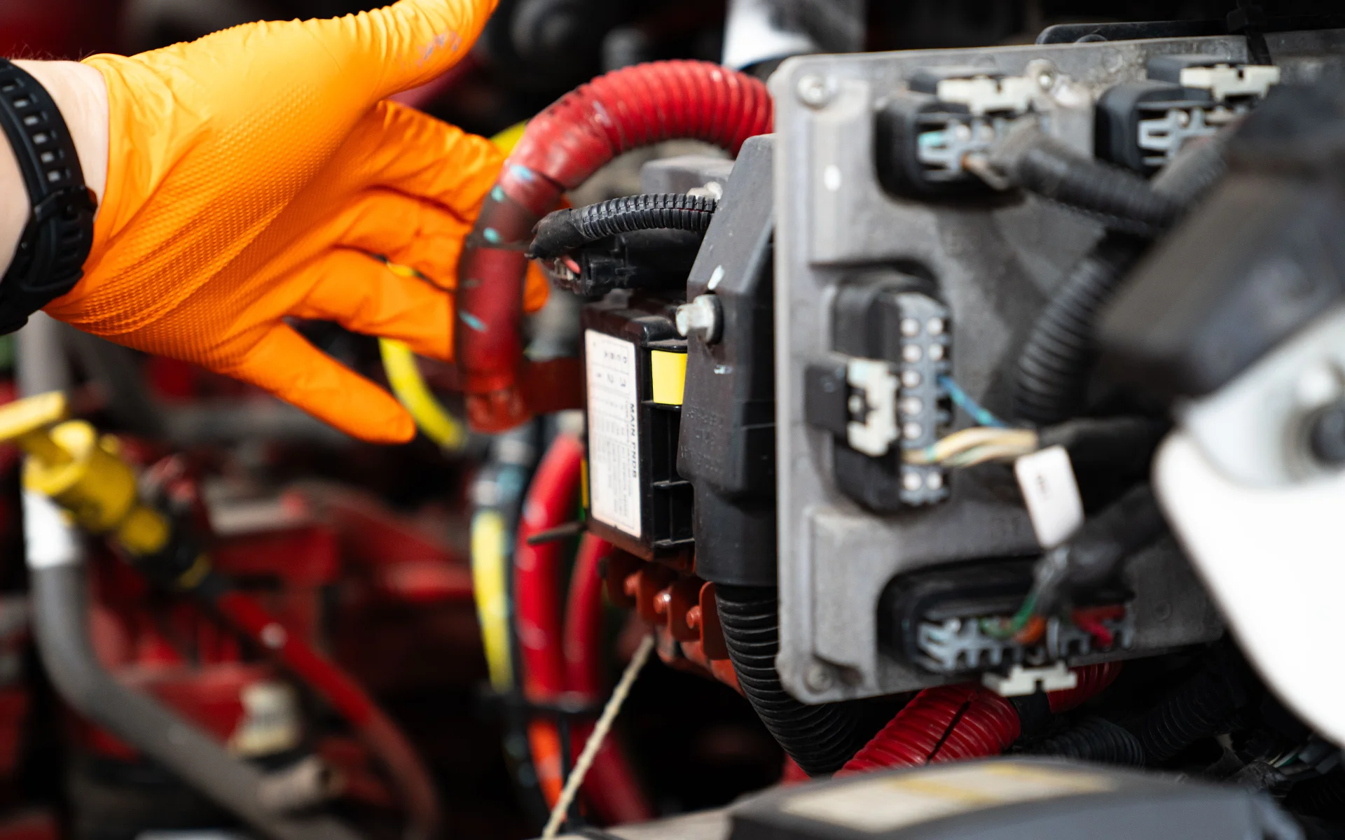 Gloved hand working on red electrical cables and components inside machinery or vehicle engine.
