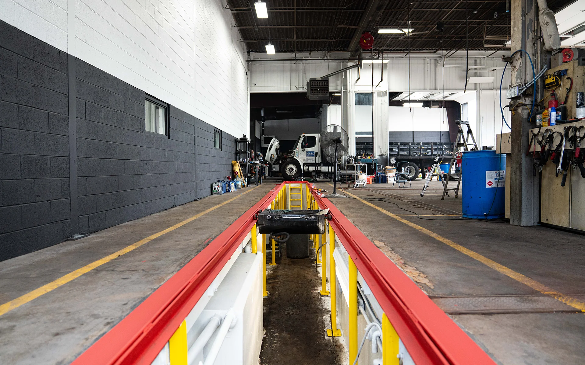 Empty vehicle inspection pit with red borders inside a clean, organized auto repair garage with a truck in background.