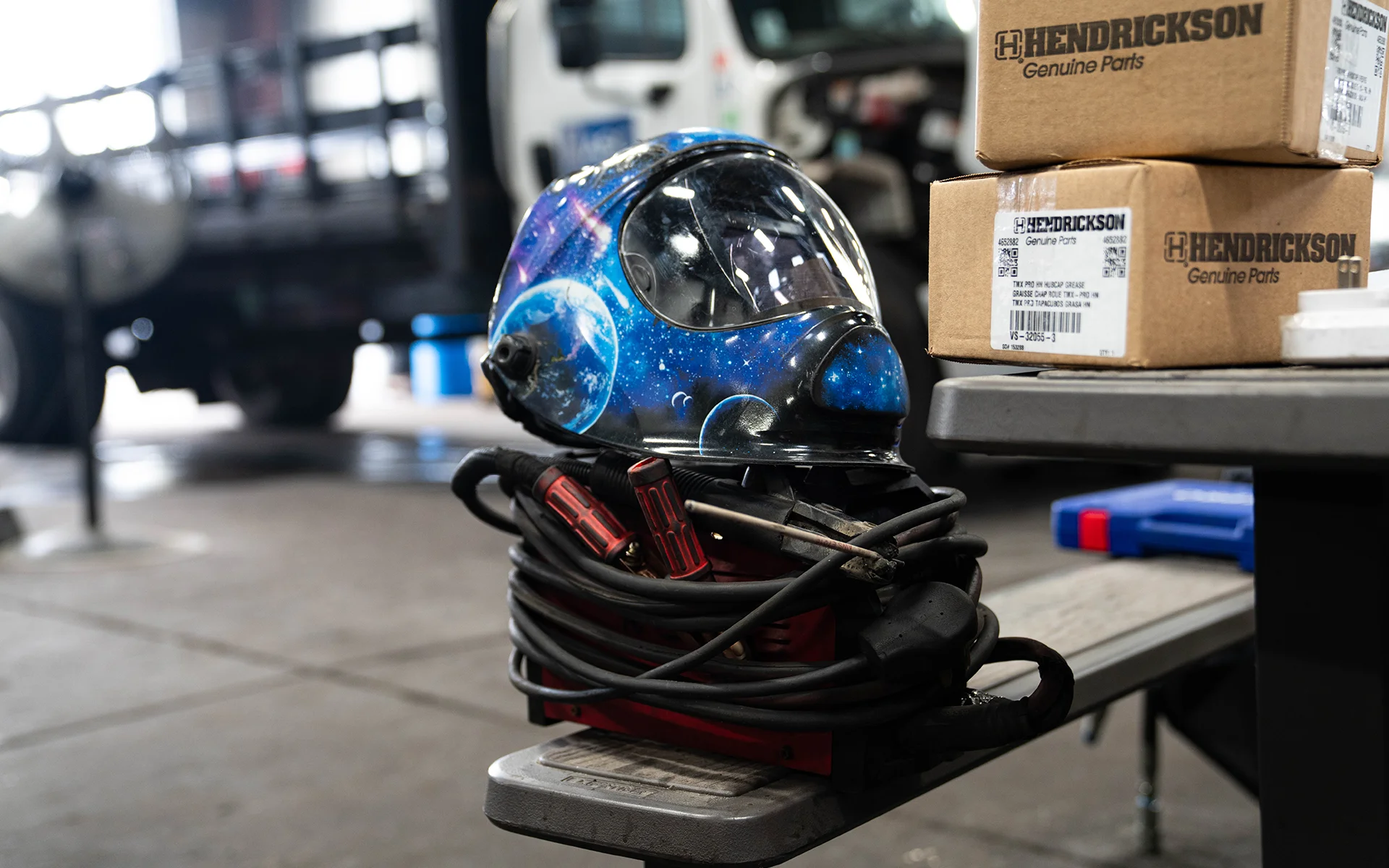 Blue welding helmet with space design resting on coiled cables and a machine beside boxes in a workshop.