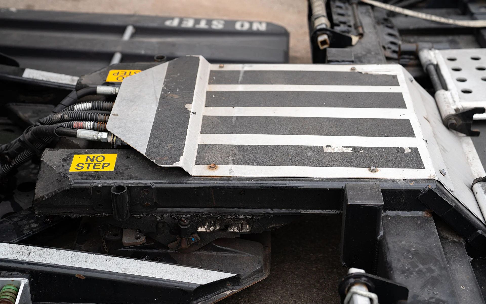 Fifth wheel trailer hitch with yellow warning label that reads 'NO STEP' on black and white metal surface.