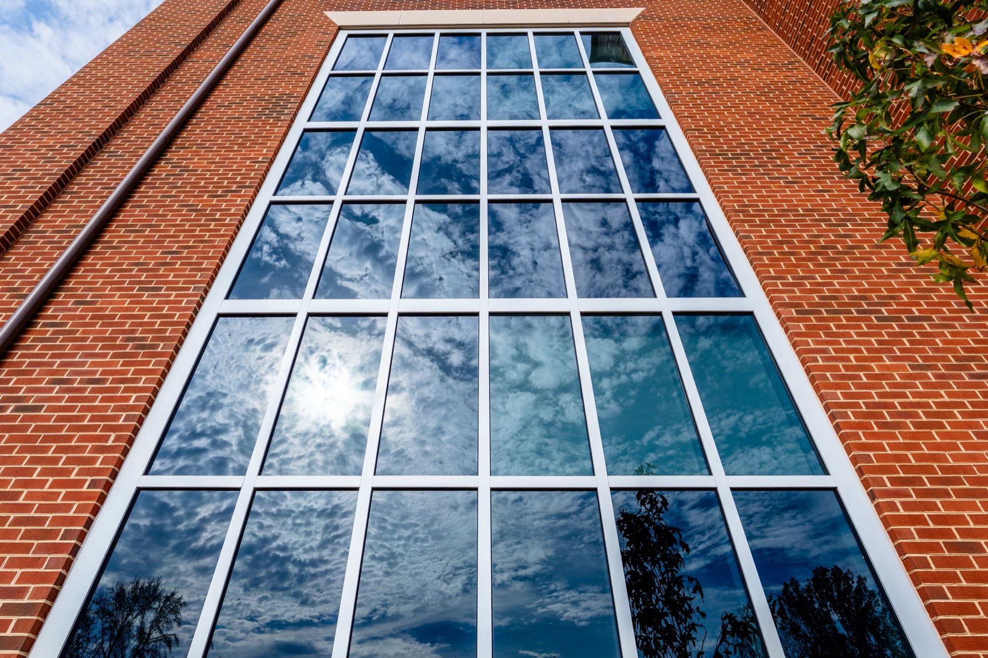 Curtain wall reflecting the sky, looking up the brick facade