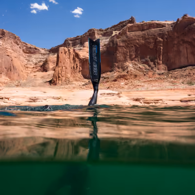 Underwater view of a kayak paddle in green water with rocky canyon cliffs and blue sky above.