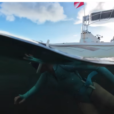 Underwater view of a snorkeler in blue gear near a boat with a red and white dive flag.