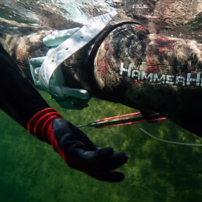 Close-up of a person underwater wearing a camo Hammerhead wetsuit and holding a speargun.
