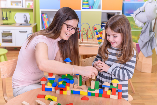 Stack of books with a red apple on top, colored pencils, and ABC blocks on a wooden table.