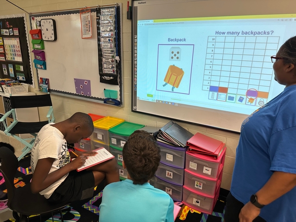 Child and adult studying a worksheet together at a yellow classroom desk.