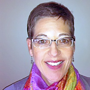 Smiling person with short hair, glasses, and a multicolored scarf on a plain background.