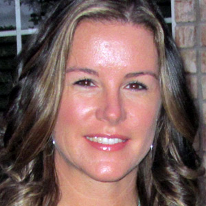 Smiling woman with wavy brown hair and natural makeup in an indoor setting.