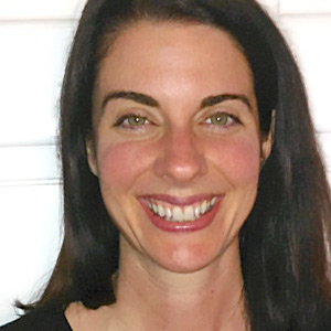 Smiling woman with long dark hair and green eyes against a light background.
