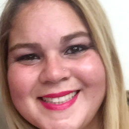Close-up of a smiling woman with long blonde hair and bright pink lipstick.
