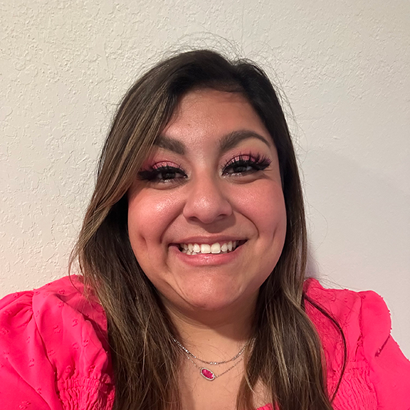 Smiling woman with long brown hair wearing pink top and matching pink eyeshadow.