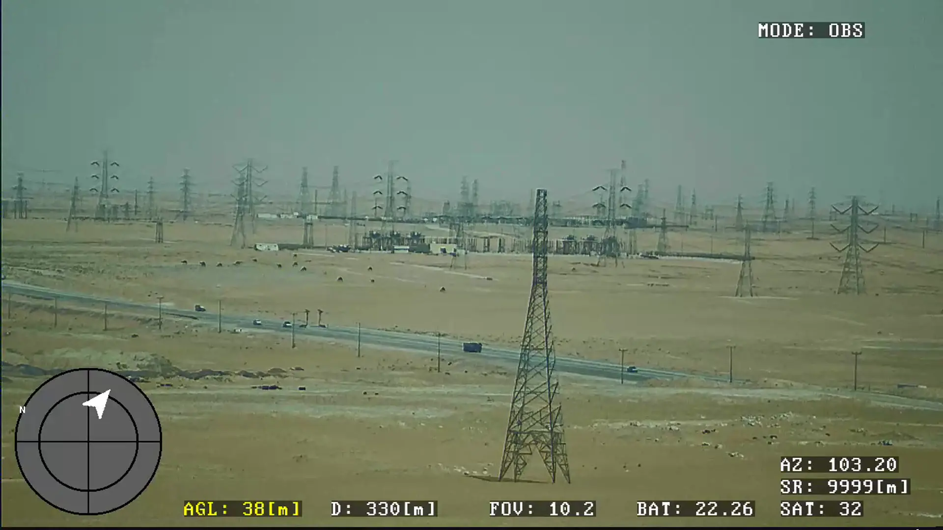 BVT516 camera feed over desert terrain showing a transmission line corridor, a substation and a highway with traffic