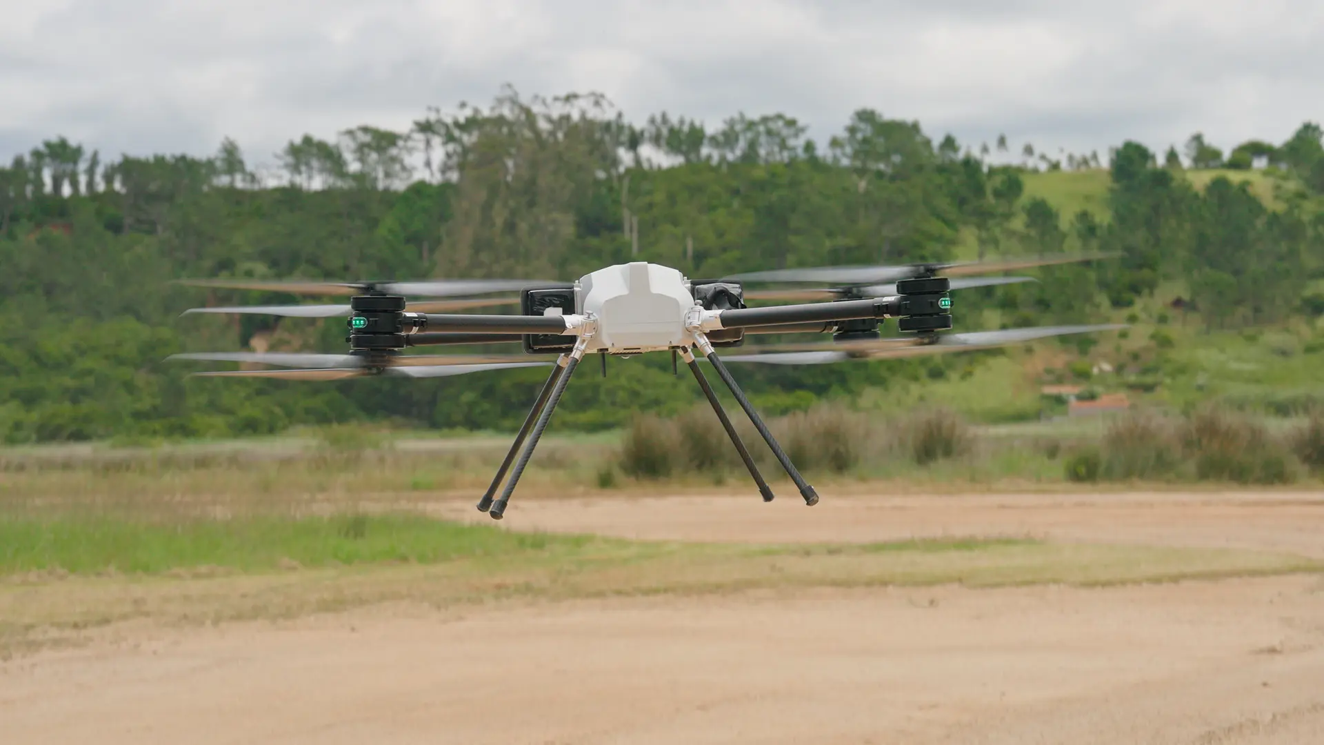 BVQ825 seen head-on hovering low over a dirt track, coaxial rotor pairs spinning, long landing legs extended