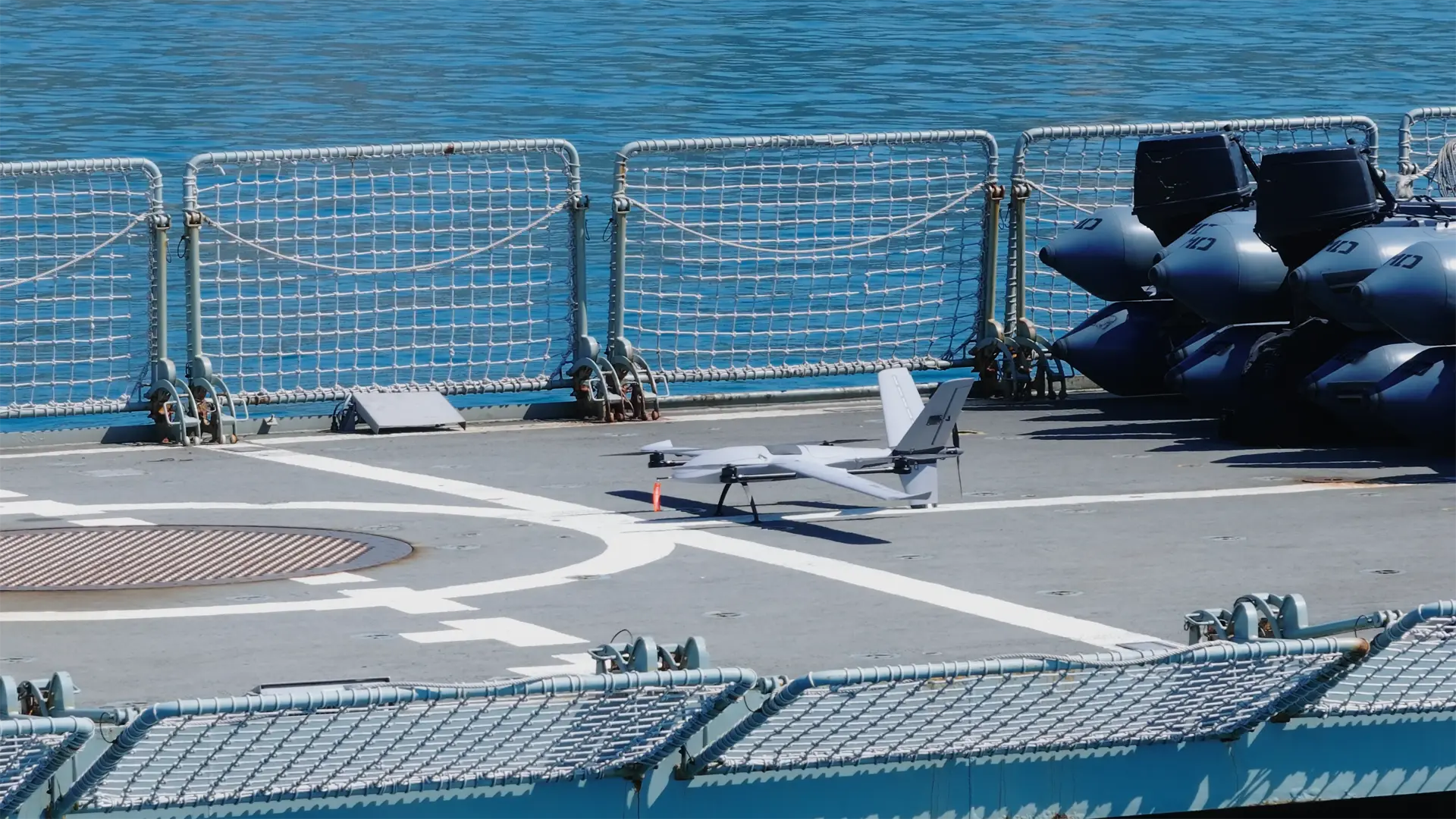 BVT516 fixed-wing drone parked on a warship flight deck, safety netting and inflatable boats along the rail