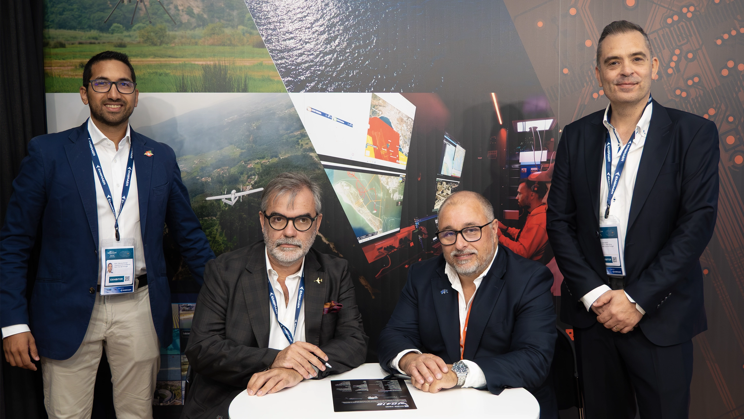 Four Beyond Vision and AVP representatives at the company stand at Farnborough, two of them seated at a table with documents.