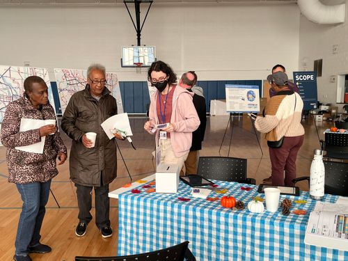 Two women are guided to a table with information by a staff member wearing a face mask